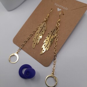May include: Gold feather earrings with a delicate chain and a small hoop at the bottom. The earrings are handmade and have a simple, elegant design.
