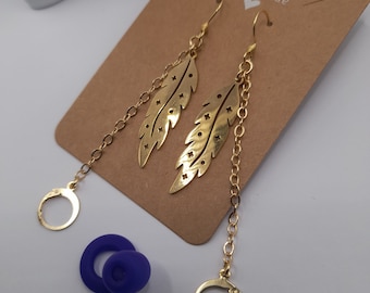May include: Gold feather earrings with a delicate chain and a small hoop at the bottom. The earrings are handmade and have a simple, elegant design.