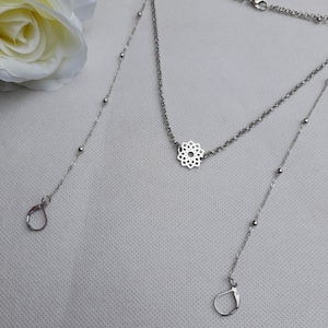 May include: A silver necklace with a delicate, intricate mandala pendant. The necklace has two chains, one with small beads and one with a more delicate chain. The necklace has two clasps, one at each end.