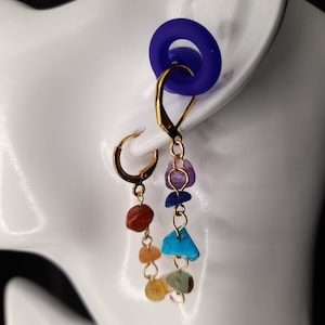 May include: Gold hoop earrings with a dangling chain of seven chakra stones. The stones are amethyst, lapis lazuli, turquoise, carnelian, citrine, aventurine, and clear quartz.