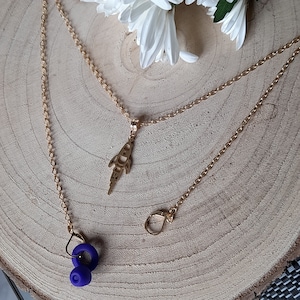 May include: A gold chain necklace with a rocket ship pendant and two purple silicone earbud holders.