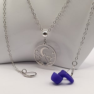 May include: A silver necklace with a round pendant featuring a crescent moon, stars, and a flame design. The necklace has a purple silicone earplug attached to the chain.