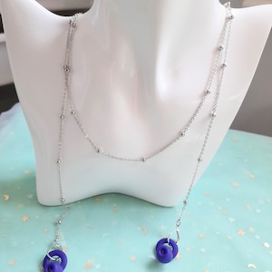May include: A silver-toned necklace with a delicate chain and small, round beads. The necklace features a Y-shaped design with a pendant of a purple ring. The jewelry is displayed on a white mannequin bust.