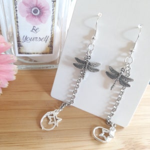 May include: Silver dangle earrings with a dragonfly charm and a star charm at the bottom of the chain.