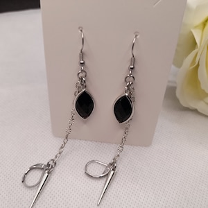 May include: A pair of silver-toned dangle earrings. Each earring features a black, teardrop-shaped gem, a delicate chain, and a long, pointed charm. The earrings are displayed against a white background.