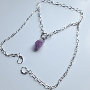 May include: A silver chain necklace with a purple amethyst crystal pendant. The necklace has two clasps, allowing it to be worn at two different lengths.