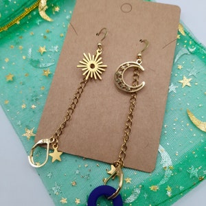 May include: Gold dangle earrings with a starburst and crescent moon design. Each earring has a chain with a star charm and a small hoop.