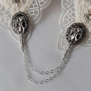 May include: A pair of white lace garters with silver skull charms and a silver chain connecting them.