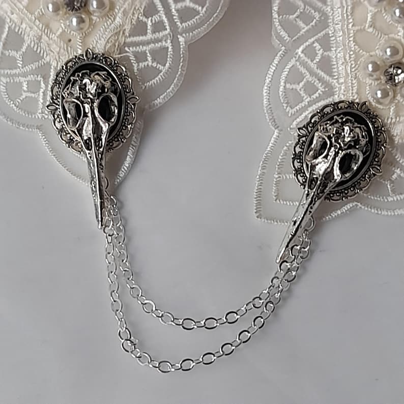 May include: A pair of white lace garters with silver skull charms and a silver chain connecting them.