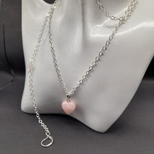 May include: A silver chain necklace with a pink heart-shaped pendant. The chain is a delicate cable style and the pendant is a smooth, polished stone.