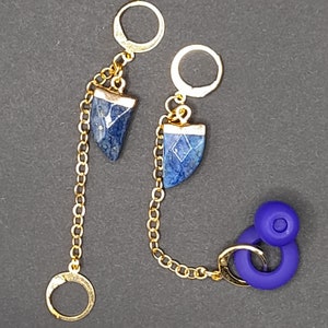 May include: A pair of gold earrings with blue stone accents. The earrings are connected by a gold chain. The earrings have a geometric design.