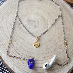 May include: A layered necklace with a gold tree of life pendant and star charms. The chain is iridescent and holds a pair of white earbuds and a purple silicone accessory.