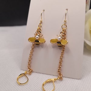May include: Gold-coloured bee earrings with yellow enamel wings and black stripes. Each bee has a small pearl accent and hangs from a delicate chain. The earrings feature a lever-back closure.