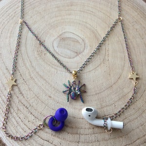 May include: A rainbow iridescent chain with gold star charms and a dangling spider charm. The chain has blue silicone earbud holders attached to each end.