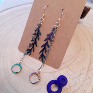 May include: A pair of iridescent earrings with a leaf design and a chain dangle. The earrings are on a brown card.