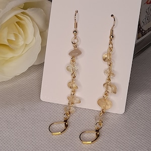 May include: A pair of dangle earrings with gold-colored hooks and chains. Each earring features a series of small, irregularly shaped, light-colored stones. The stones are connected by gold-colored chain links, creating a cascading effect.