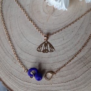May include: A gold chain necklace with a butterfly pendant and two blue earbud holders. The necklace is on a wooden surface.