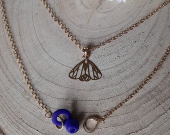 May include: A gold chain necklace with a butterfly pendant and two blue earbud holders. The necklace is on a wooden surface.