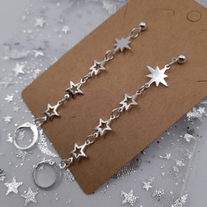 May include: A pair of silver star-shaped dangle earrings with hoop closures. Each earring features a chain with five star charms and a larger star charm at the top.
