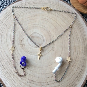 May include: A gold chain necklace with star charms and a small gold cross pendant. The necklace is attached to a pair of white wireless earbuds and a pair of blue silicone earbud tips.