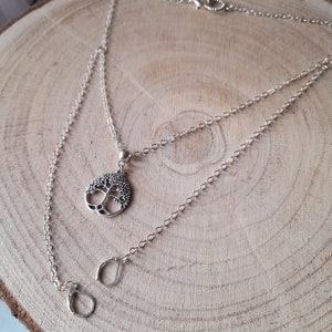 May include: A silver chain necklace with a tree of life pendant. The necklace is layered and has two chains.