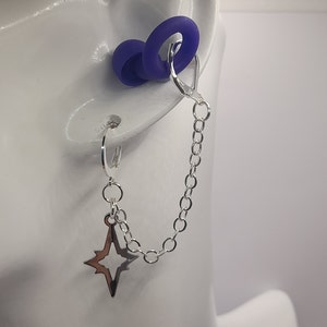 May include: A silver chain earring with a star charm. The earring is attached to a clear ear cuff with a purple silicone ear plug.