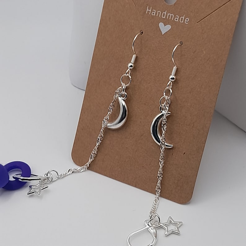 Moon and star charm loop earplug earrings with a loop earplug attached to the leverback clip on the end of one of the earring chains. The earrings are displayed on a kraft card placed against a white background.
