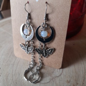 以下が含まれることがあります： 三日月型のチャーム、小さな白いビーズ、そして精巧な銀製の蝶のチャームが付いたシルバー製のドロップイヤリングです。