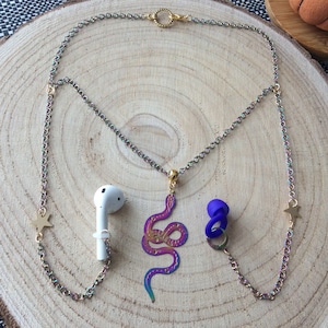 May include: A rainbow iridescent chain necklace with a snake charm, two star charms, and two earbud holders. The earbud holders are made of clear plastic and blue silicone.