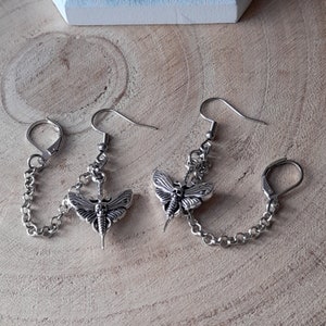 May include: A pair of silver chain earrings with a butterfly pendant. Each butterfly has a skull design and intricate details.
