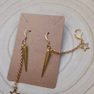 May include: Gold earrings with a sharp, pointed design and a dangling chain with a star charm.