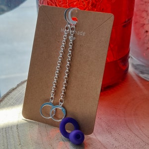 Könnte beinhalten: Ein Paar silberne Kettenohrringe mit einem violetten Kreisanhänger. Die Ohrringe befinden sich auf einer braunen Karte mit dem Wort "Handmade" darauf.