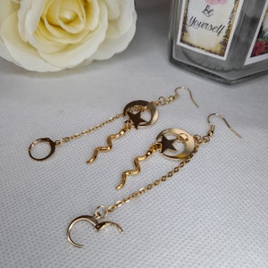 May include: Gold tone earrings with a crescent moon and star charm dangling from a chain with a snake-like detail. The earrings have a hoop closure.