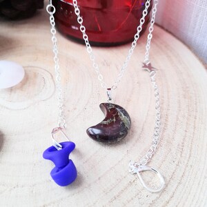 May include: A silver chain necklace with a crescent moon pendant made of red and green jasper. The pendant is attached to a silver chain with a lobster clasp. The necklace is also attached to a silver chain with a star charm.