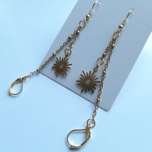 May include: A pair of gold dangle earrings with a starburst design. The earrings have a hook closure and a long chain with small beads.