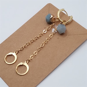 May include: Gold hoop earrings with a delicate chain and two light blue gemstone accents.