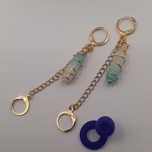 Könnte beinhalten: Ein Paar goldene Ohrringe mit einem blauen und weißen Kristallanhänger an jedem Ohrring. Die Ohrringe sind mit einer goldenen Kette verbunden, die oben einen goldenen Ring hat.