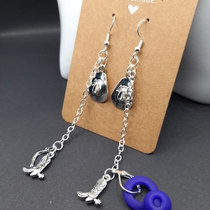 May include: Silver dangle earrings featuring a cowboy hat charm and a cowboy boot charm. The earrings are displayed on a brown card with the word "handmade" written on it.