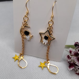 May include: Gold dangle earrings with a crescent moon, a star, and a small astronaut charm. The charms are attached to a gold chain.