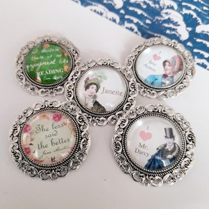 Könnte beinhalten: Fünf silberfarbene runde Broschen mit Glaseinsätzen, die Zitate und Illustrationen von Jane Austen zeigen. Die Broschen haben verzierte Filigranmuster an den Rändern.