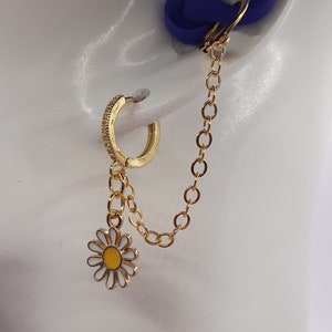 May include: Gold hoop earring with a small daisy charm hanging from a chain. The earring is on a white mannequin head.