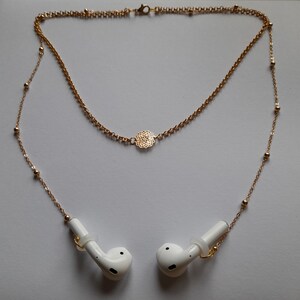 May include: A gold chain necklace with a decorative pendant and two white earbud holders attached.