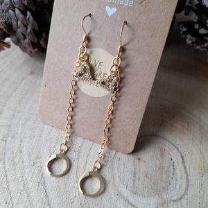 May include: Gold earrings with a dangling chain and a heart charm with clear rhinestones. The earrings are on a brown card with the text "Handmade" and "Live, Love, Create" on it.