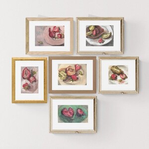 Puede incluir: Una colección de pinturas en acuarela enmarcadas que presentan composiciones de naturaleza muerta de frutas. Las pinturas representan fresas, melocotones y kiwis en platos. Los marcos son de varios estilos, incluyendo dorado y madera natural, sobre una pared blanca.