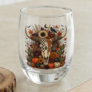 Glass tumbler with bull skull adorned with autumn foliage and pumpkins.