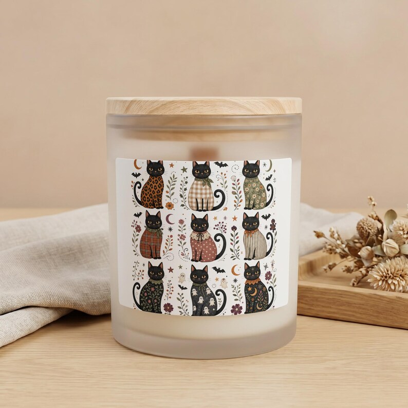 Candle with a frosted glass jar and wooden lid featuring a label with nine illustrated black cats.
