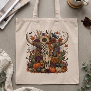 Tote bag featuring a decorated bull skull with autumn flowers, pumpkins, and bats.