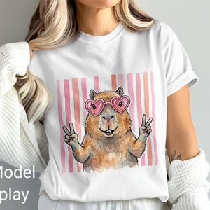 Capybara wearing heart sunglasses and holding up peace signs, with pink stripes.