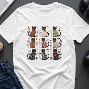 White t-shirt with a grid of nine black cats with fall-themed patterns and Halloween motifs.