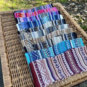 May include: A selection of patterned headbands in a wicker basket. The headbands display geometric designs in shades of pink, blue, purple, and brown. The headbands are made of a woven material, and are arranged in a neat row.